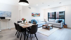 A modern living room with a dining area, a sofa, and a coffee table. There is a map on the wall and a painting above the sofa. - Revelstoke - Bluebird- New condo! (Revelstoke)