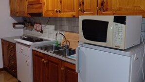 Een keuken met houten kasten, een witte magnetron en een spoelbak.