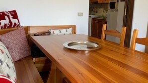 Een gezellig eetgedeelte met een houten tafel, bankjes, en een keuken in de achtergrond.