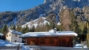 Een houten chalet met een met sneeuw bedekte dak, omringd door een besneeuwd landschap en bergen op de achtergrond.
