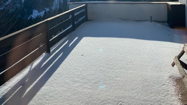 Een sneeuwbedekt balkon met houten hekwerk met uitzicht op een bergachtig landschap.