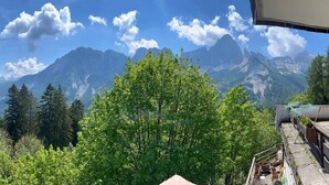 Bergzicht vanaf een balkon met houten reling en een stenen vloer.
