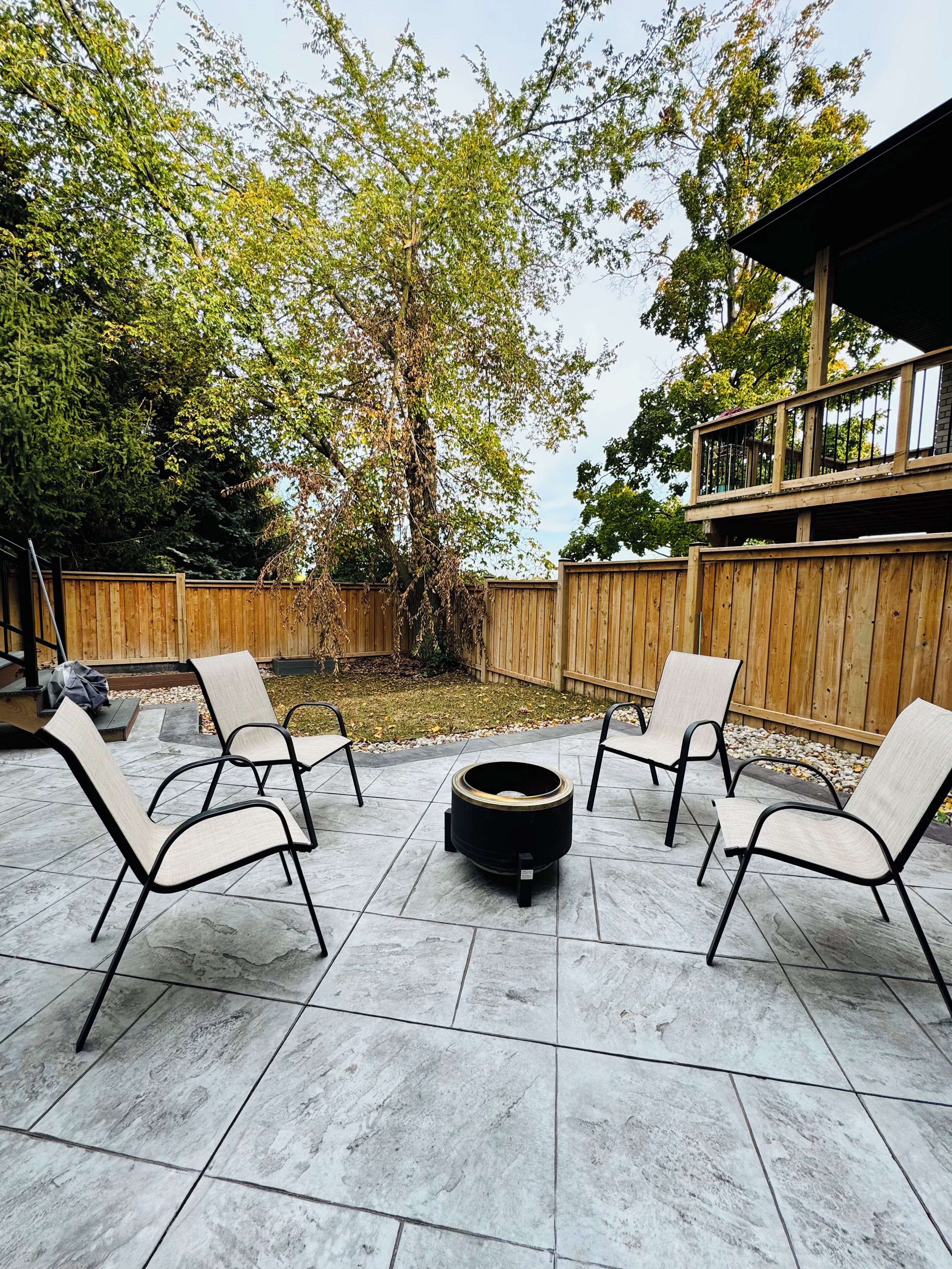 Eine Terrasse mit vier Stühlen, die um eine Feuerstelle angeordnet sind, ein Holzdeck und ein Holzzaun im Hintergrund.