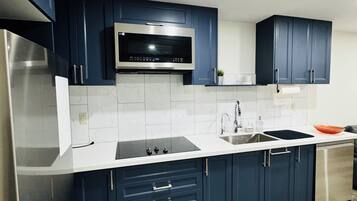 Une cuisine moderne avec des meubles bleu foncé, des plans de travail blancs, un réfrigérateur en acier inoxydable, un four à micro-ondes et un lave-vaisselle.