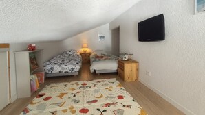 Un dormitorio acogedor en el ático con dos camas, un televisor y una mesita de noche de madera.