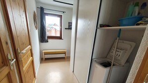 Un pasillo estrecho con un banco de madera, una ventana que ofrece vistas a edificios y un estante con productos de limpieza.