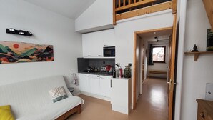 Un espacio habitable compacto con kitchenette, un sofá, un cuadro y una zona superior tipo altillo.