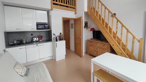 Una cocina compacta con armarios blancos, un microondas y un tostador. Hay una escalera de madera con una lámpara roja en el descansillo.
