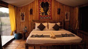 A wooden room with a bed, curtains, and a wall hanging. - Maisha Serengeti Camps (Serengeti)
