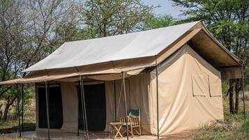 Tenda de safári com entrada coberta, uma cadeira e vista desobstruída para as árvores ao redor.