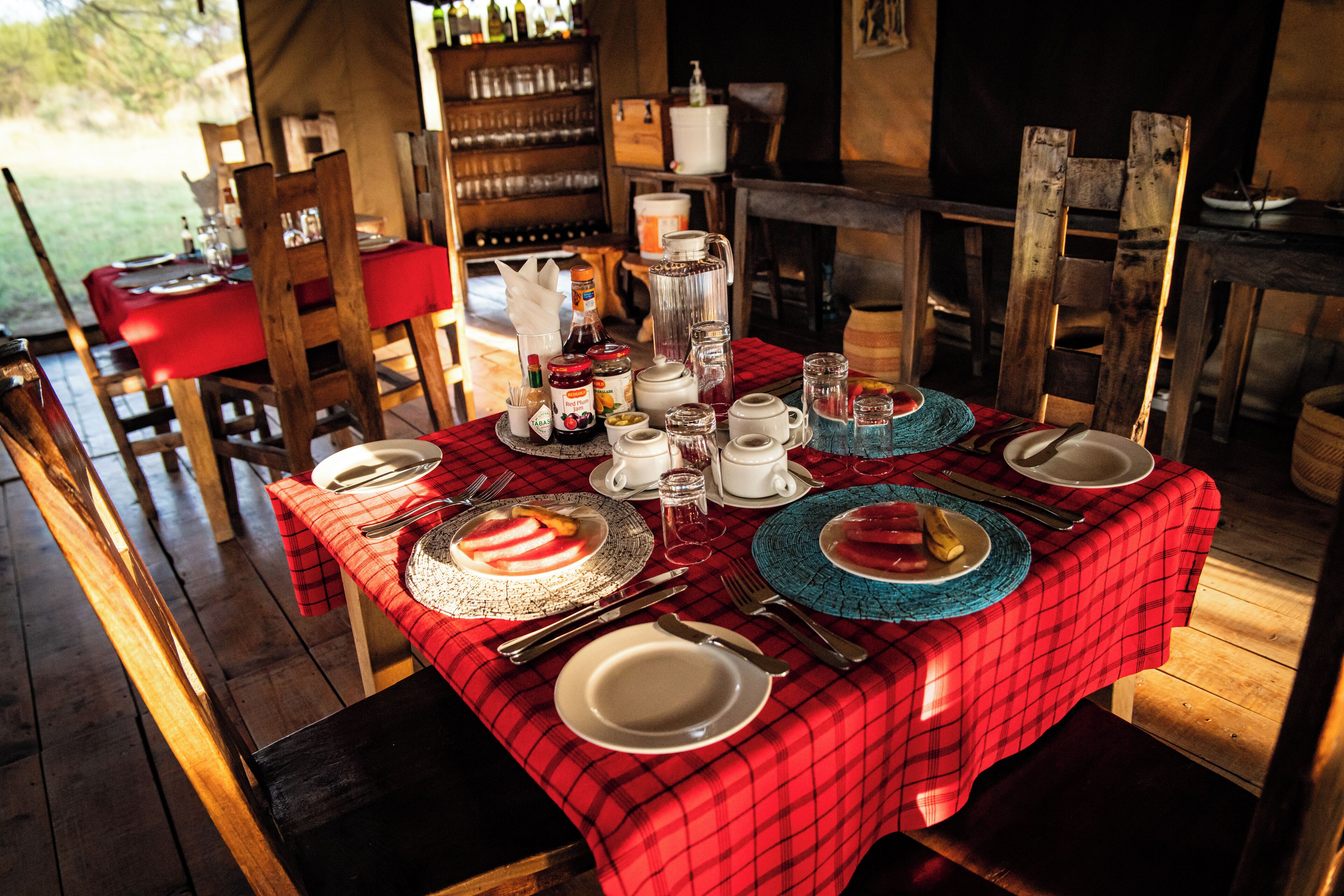 A dining table set for four with a red plaid tablecloth, white plates, and various glassware.
