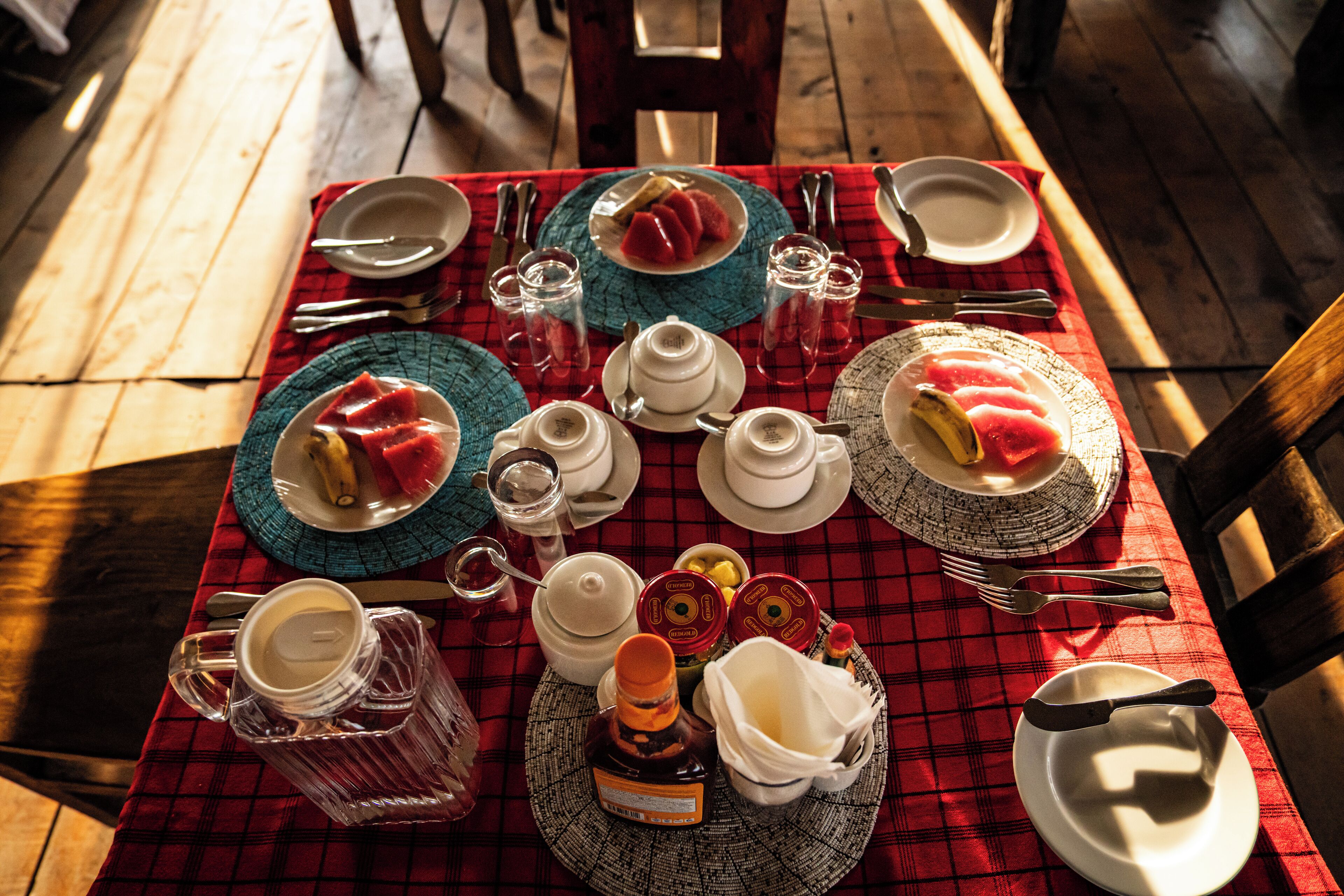 Una mesa dispuesta con platos, tazones, vasos y cubiertos, sobre un mantel a cuadros rojos.