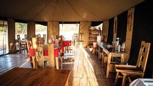A tented dining area with wooden tables and chairs, a bar with bottles, and a view of the outdoors. - Maisha Serengeti Camps (Serengeti)