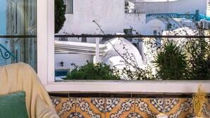 Un balcón con vista al mar y edificios blancos, un sofá color beige y un salpicadero de azulejos estampados.