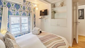Une chambre à coucher comprenant un lit, une fenêtre, un téléviseur et une étagère avec des objets décoratifs.