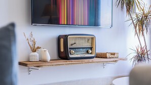A vintage radio on a wooden shelf, a vase with dried plants, and a colorful striped artwork on the wall. - La Vague Bleue – water feet S 04 (Marsa)