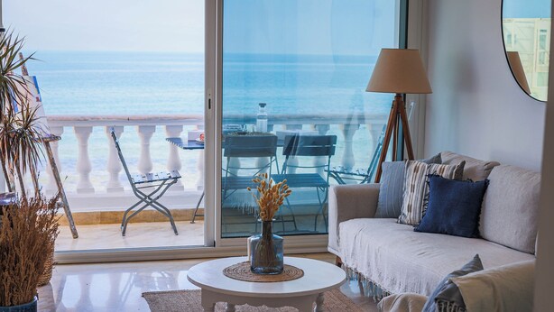 A living room with a view of the sea, a white sofa, a coffee table, and a lamp. - La Vague Bleue – water feet S 04 (Marsa)