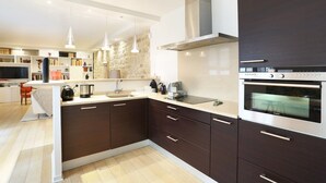 A modern kitchen with dark cabinetry, a built-in oven, and pendant lighting. - Chic Apartment & Terrace Eiffel Tower - Trocadero (Paris)