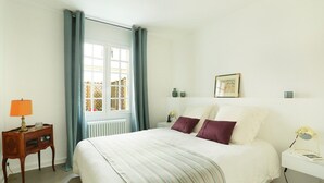 A neatly arranged bedroom with a bed, bedside tables, a lamp, and a window with curtains. - Chic Apartment & Terrace Eiffel Tower - Trocadero (Paris)