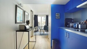 Een moderne keuken met een blauwe accentmuur, een eethoek met tafel en stoelen, en een gang naar een balkon.