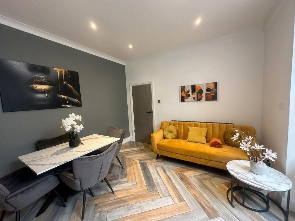 A modern living room with a dining area, featuring a sofa, a dining table with chairs, and artwork on the walls.