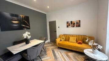 A modern living room with a dining area, featuring a sofa, a dining table with chairs, and artwork on the walls.