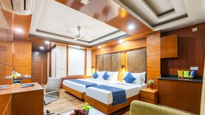 Une chambre d’hôtel avec deux lits, un bureau, une chaise, une petite table avec des fruits et une kitchenette.