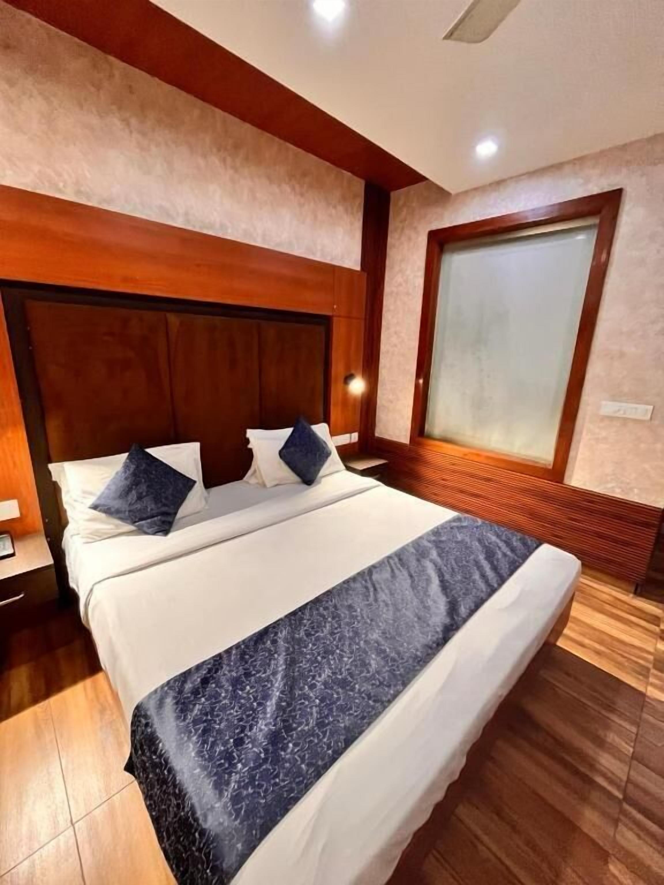 A neatly made bed with a wooden headboard, a large window with frosted glass, and a wooden floor.