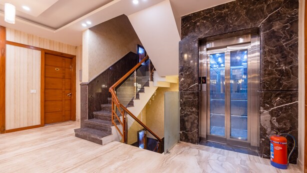 Un intérieur moderne avec un escalier en marbre, une porte en bois et un ascenseur en verre.