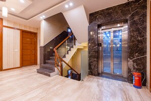 Un interior moderno con una escalera de mármol, una puerta de madera y un ascensor de vidrio.