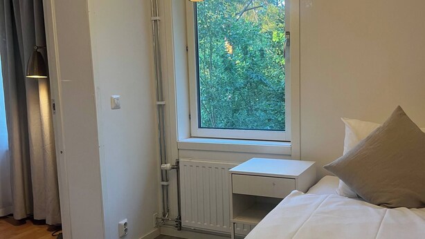 Camera da letto con un letto, una finestra vista verde, un termosifone e una lampada a sospensione.