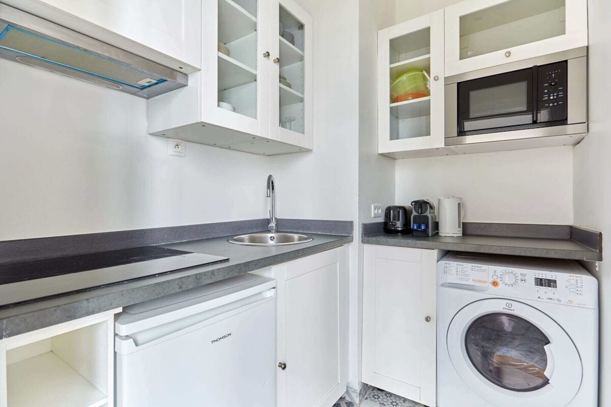 Une cuisine compacte équipée d’un four à micro-ondes encastré, d’un lave-linge et d’un évier.