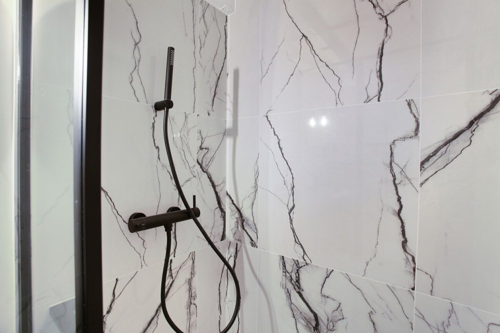 A bathroom with white marble tiles and a shower area with a black hose.