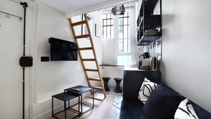 Ein modernes Wohnzimmer mit einem schwarzen Sofa, einer Holzleiter, einem kleinen schwarzen Tisch und einem an der Wand montierten Fernseher.