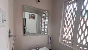 Ein Badezimmer mit weißem Waschbecken, einem Spiegel, einer Dusche und einem Fenster mit Gitterwerk.