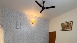 Ein geräumiges Zimmer mit Deckenventilator, gemustertem Wandpapier, einem gerahmten Gemälde und einem grün gestreiften Teppich.
