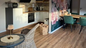 Una cocina moderna con armarios blancos, un microondas y una estufa. Hay un comedor con una mesa y sillas, y un gran mural floral en la pared.