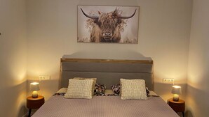 Un dormitorio con una cama grande, dos mesitas de noche, una araña y una obra de arte con motivos taurinos en la pared.