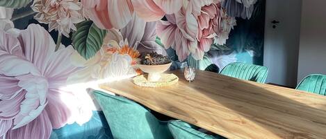 Un comedor con una mesa de madera, sillas color turquesa y un mural floral en la pared.