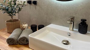 Un baño con un lavamanos blanco, un espejo redondo con marco negro, una planta en maceta y dos toallas enrolladas sobre una encimera de madera.