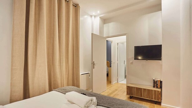 Une chambre à coucher avec un lit, un téléviseur fixé au mur et un banc avec des livres.
