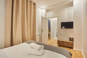 A bedroom with a bed, a TV mounted on the wall, and a bench with books. - Charming apartment - Center of Paris (Paris)