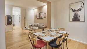 Un coin repas avec une table dressée pour quatre personnes, un canapé et une œuvre d’art représentant un cerf, accrochée au mur.
