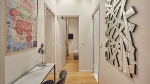 Un couloir comprenant un bureau, des chaises, une lampe, une peinture abstraite aux couleurs vives et une œuvre d’art géométrique fixée au mur.