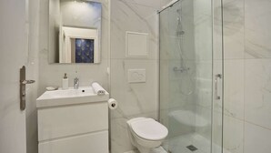 Une salle de bain moderne avec une douche à parois de verre, un lavabo blanc avec un miroir au-dessus et des toilettes.