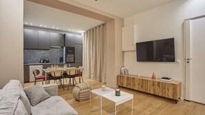 Un salon moderne avec un canapé gris, un coin repas avec une table et des chaises, une cuisine avec des meubles gris et un téléviseur fixé au mur.