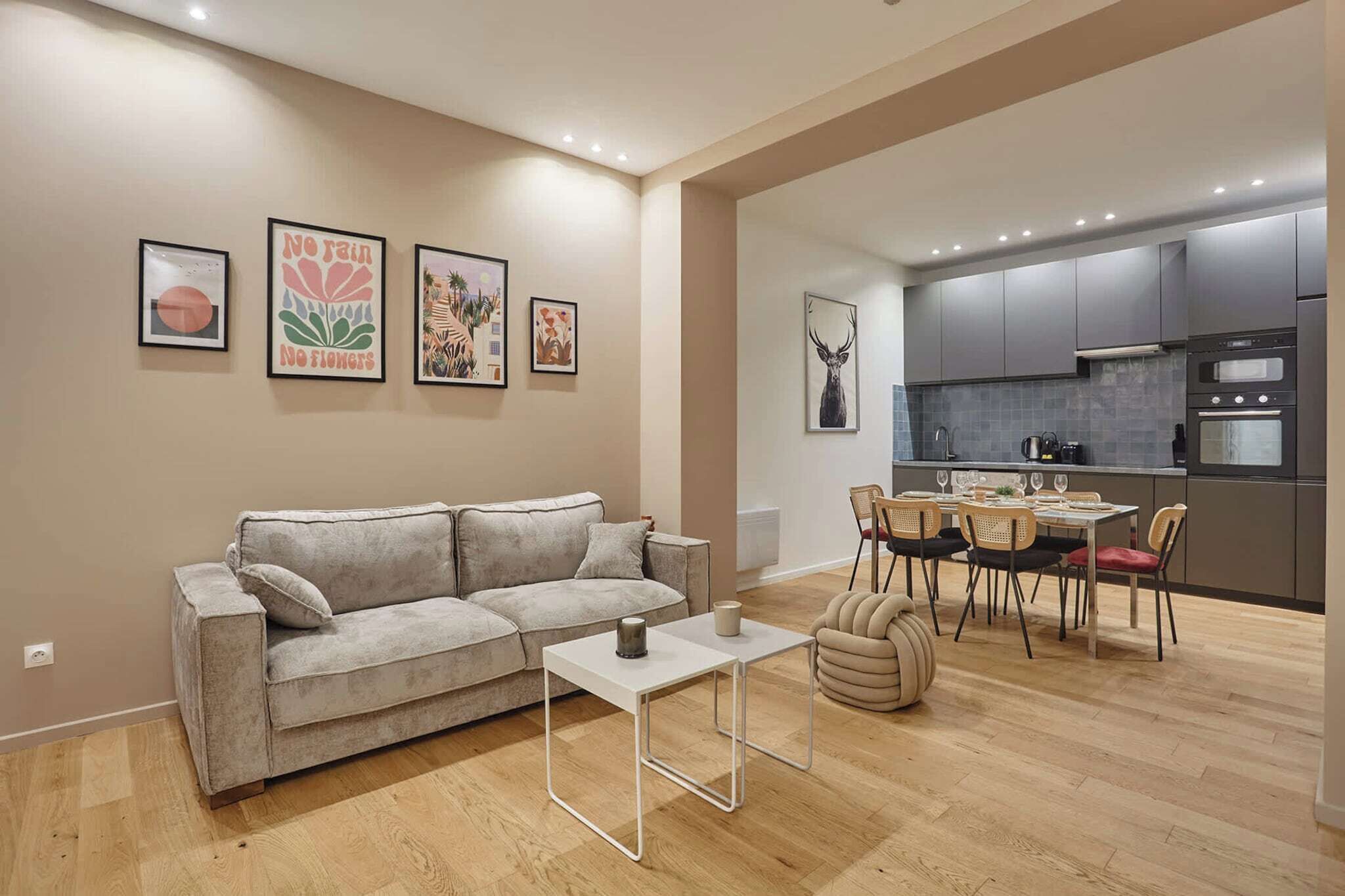 A modern living room with a grey sofa, a small white table, and a dining area with chairs and a table set for two.