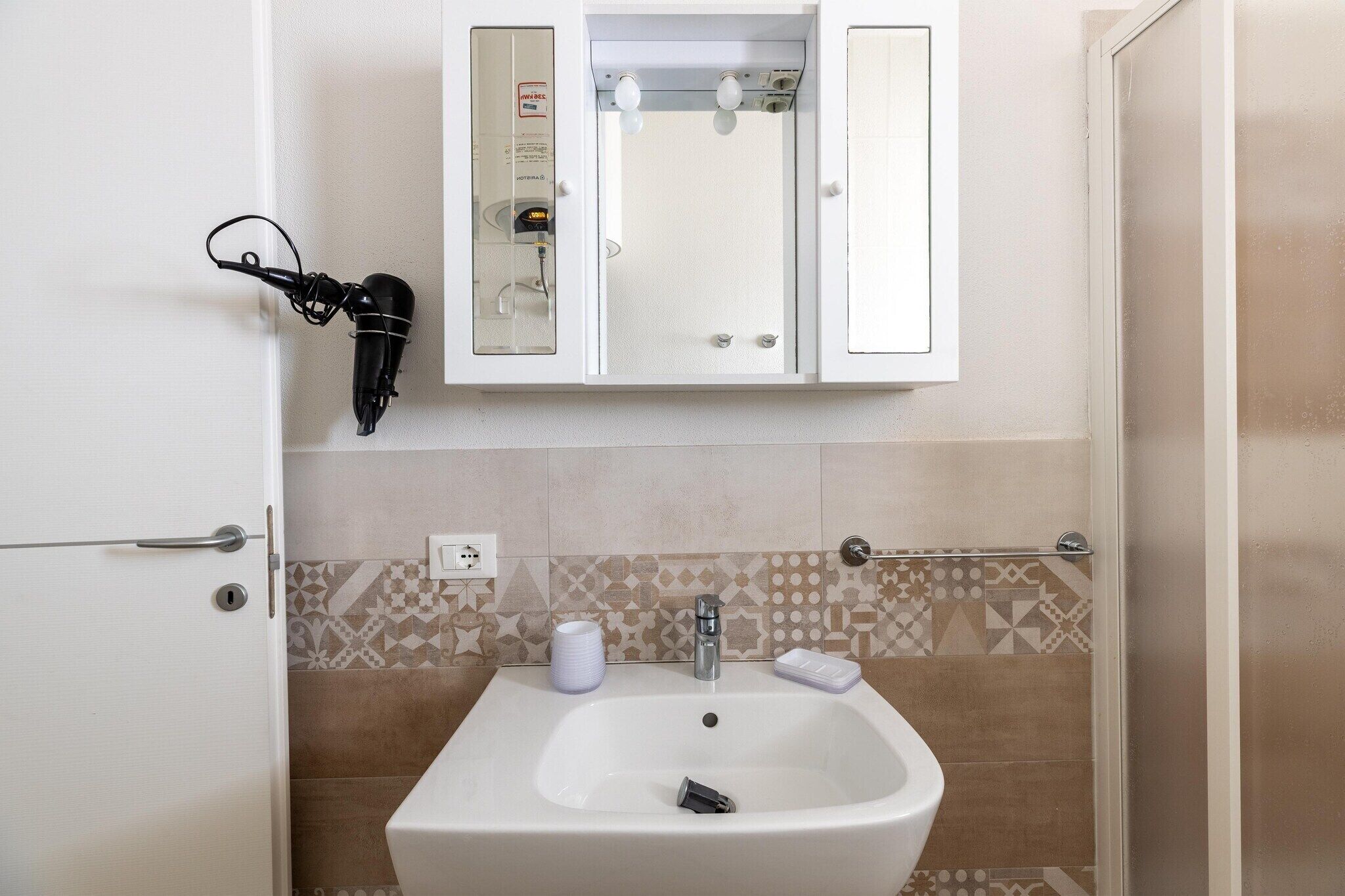 Une salle de bain avec un lavabo blanc, un meuble à miroir et des carreaux à motifs.