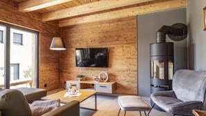 Un salon chaleureux avec un mur en bois, un téléviseur à écran plat, un canapé, un fauteuil et une cheminée.
