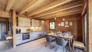 Une cuisine moderne avec des poutres en bois, un coin repas avec une table et des chaises en bois, et une grande fenêtre.